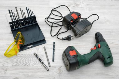 Akülü matkap, yedek bir batarya, birtakım bit ve ahşap masa zemin üzerine sarı koruyucu gözlük.