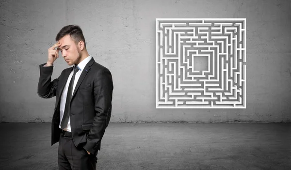 Um homem de negócios em pensamento profundo com um labirinto branco no fundo de concreto atrás dele . — Fotografia de Stock