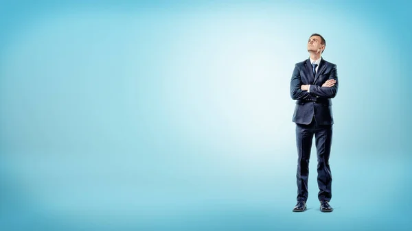 Een zakenman op blauwe achtergrond staan met handen gekruist diep in gedachte. — Stockfoto