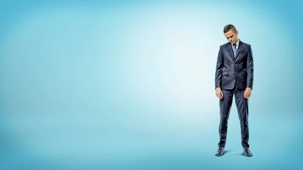 Un uomo d'affari depresso in piedi con le spalle piegate su sfondo blu . — Foto Stock