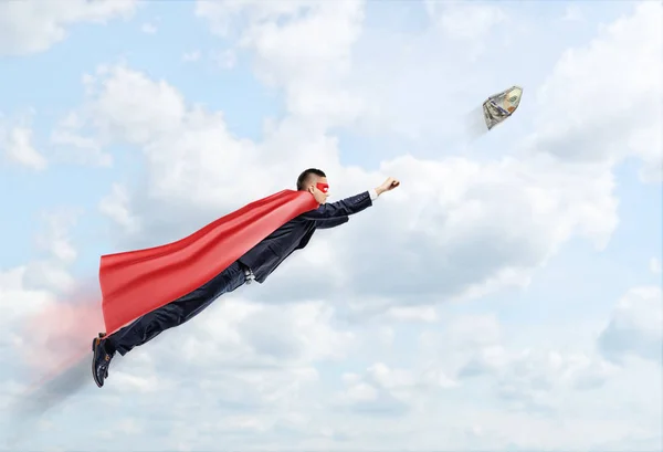 Een zakenman in een superheld Kaap vliegen in de lucht proberen te vangen van een bankbiljet van 100 Usd. — Stockfoto