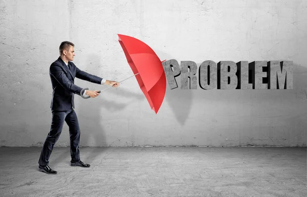 Een zakenman verstopt achter een rode open paraplu van een woord probleem op de muur. — Stockfoto