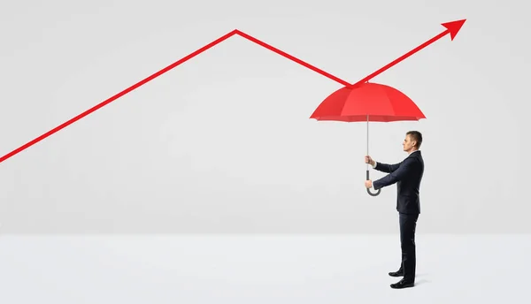 Ein Geschäftsmann hält einen roten Regenschirm direkt unter einem roten Statistikpfeil, der nach oben zeigt. — Stockfoto