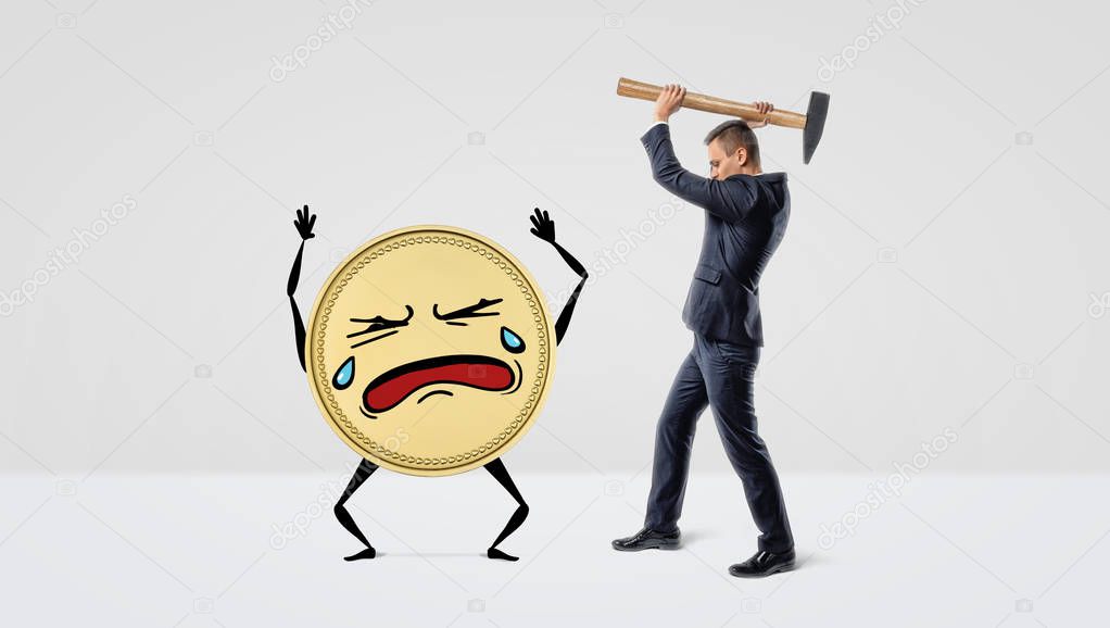 A businessman holding a large hammer over a golden coin with arms, legs and a crying face.