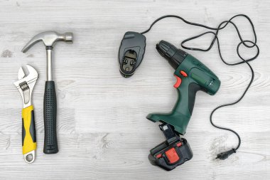 Akülü matkap, o bir çekiç ve anahtarla ahşap masa arka plan üzerinde yanında şarj cihazı.