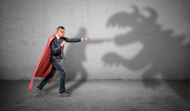 A superhero businessman fighting off a dragon shadow on concrete background. clipart