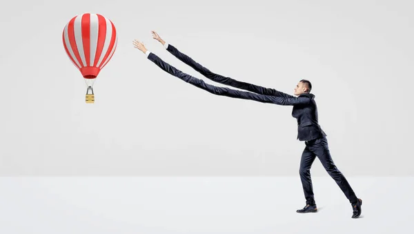 Een zakenman in zijaanzicht proberen te vangen een grote vliegen-luchtballon met zijn extra lange armen. — Stockfoto