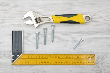 Sarı açı cetvel, bir İngiliz anahtarı ve hafif ahşap masa üzerinde yerleştirilen dört vida cıvata.