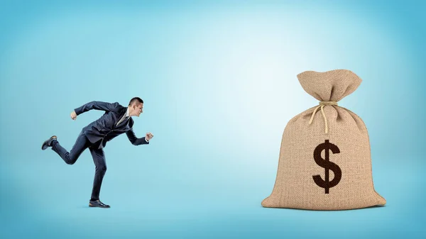 Um pequeno homem de negócios a correr para um saco gigante fechado com um sinal de dólar. . — Fotografia de Stock