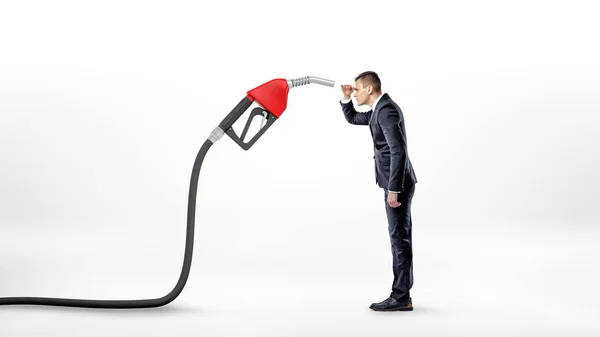 A businessman on white background staring closely at a large red gas nozzle attached to a black hose. — Stock Photo, Image