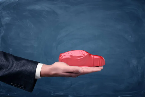 Een hand van de businessmans met een silhouet van de auto bedekt met een rode golvende weefsel. — Stockfoto