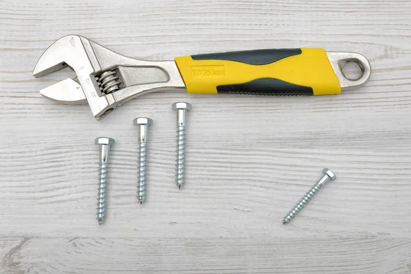 A yellow wrench and four screw bolts placed on light wooden table. — Stock Photo, Image