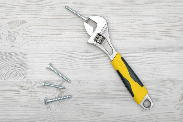 Una llave amarilla y cuatro tornillos colocados sobre una mesa de madera ligera . —  Fotos de Stock