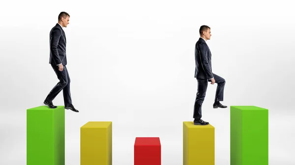 Dos hombres de negocios sobre fondo blanco subiendo y bajando columnas estadísticas verdes, amarillas y verdes . — Foto de Stock