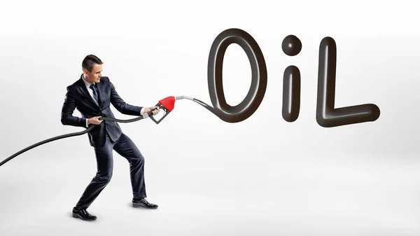 A businessman holds a gas nozzle and writes a large word Oil on white background.