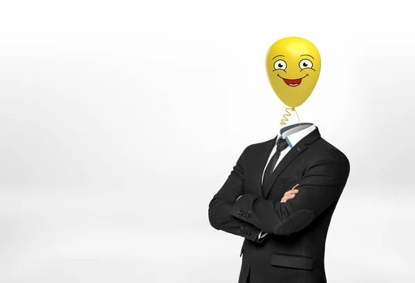 Um homem de negócios no fundo branco fica com as mãos cruzadas e um balão de rosto amarelo feliz em vez de sua cabeça . — Fotografia de Stock