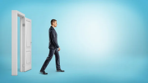 Un hombre de negocios sobre fondo azul caminando a través de un marco de puerta blanco abierto . — Foto de Stock