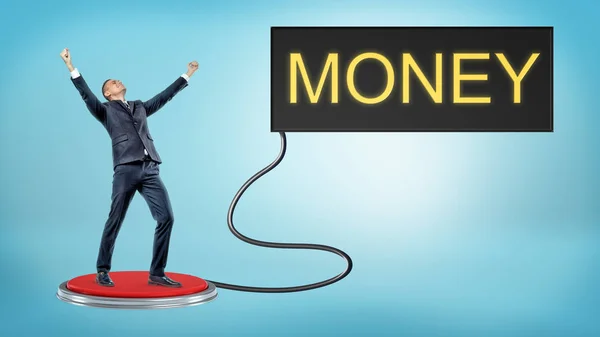 Переможний бізнесмен стоїть на великій червоній кнопці, яка з'єднана з монітором зі словом MONEY . — стокове фото