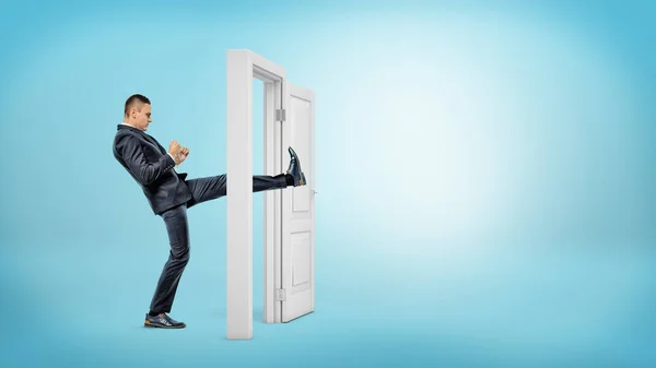 Um homem de negócios em vista lateral chuta uma pequena porta branca aberta com a perna em fundos azuis . — Fotografia de Stock