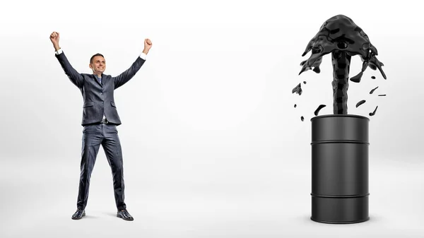 Egy boldog üzletember mellett egy fekete hordó, amely erős olaj áramlik ki belőle. — Stock Fotó