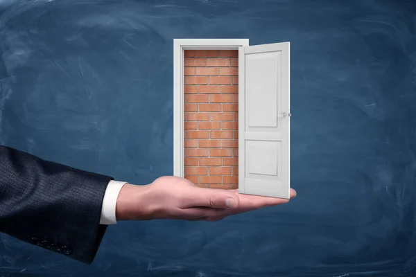 Una pequeña puerta blanca se abre para mostrar una pared de ladrillo que se encuentra en una palma de negocios . — Foto de Stock