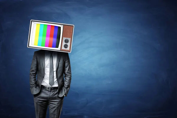 Ein ruhiger Geschäftsmann mit den Händen in den Taschen trägt eine alte Fernsehbox mit Farbbalken auf dem Bildschirm. — Stockfoto