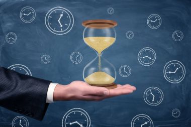 Bir businessmans el döndü kadar palmiye ve Beklemeler mavi kara tahta arka plan üzerinde büyük işleyen kum saati.