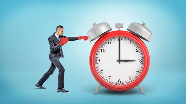 A little businessman wears boxing gloves and punches a giant red alarm clock. — Stock Photo, Image