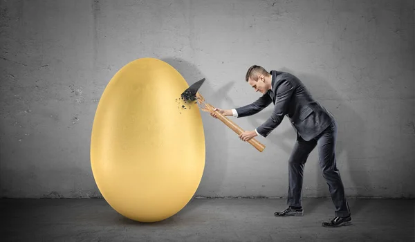 Бизнесмен не разбивает гигантское золотое яйцо, потому что его молоток разбивается на куски. . — стоковое фото