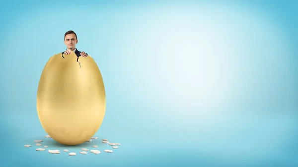 Um homem de negócios feliz olha de dentro de um ovo dourado gigante com um topo quebrado . — Fotografia de Stock