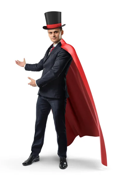 Un hombre de negocios con una capa roja y un gran sombrero de ilusionistas muestra algo sobre un fondo blanco . —  Fotos de Stock