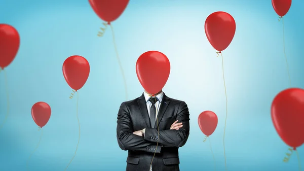 Een zakenman aan de voorzijde uitzicht met gekruiste armen staat omgeven door vele rode feest ballonnen met één verbergen van zijn gezicht. — Stockfoto