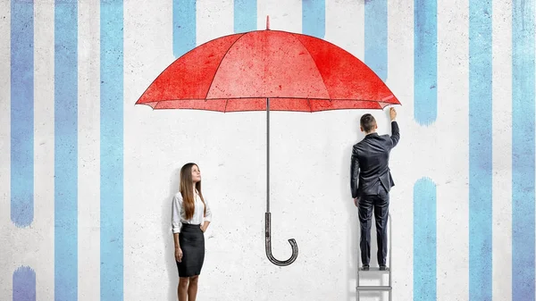 Een zakenvrouw staat in de buurt van een muur waar een zakenman trekt een gigantische rode paraplu die hen van de regen. — Stockfoto