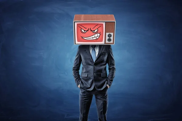 En självsäker affärsman har sina händer i fickor och bär en gammal Tv med en arg smiley ansikte på huvudet. — Stockfoto