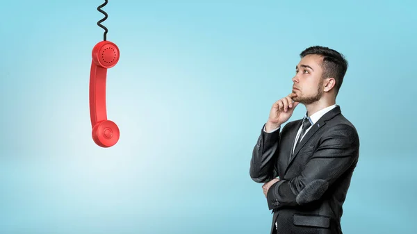 Een zakenman denken opgezocht op een rode retro telefoon ontvanger opknoping van een zwarte koord. — Stockfoto