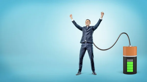 Egy boldog üzletember emelt kézzel kapcsolódik egy nagy akkumulátor, töltési őt. — Stock Fotó