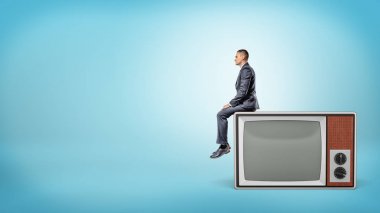 Küçük bir iş adamı yan görünümü ile boş ekran dev retro televizyon üzerinde oturuyor.