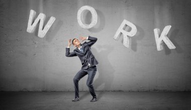 Korkmuş bir işadamı bir kelime iş onu yukarıda gri bir arka plan üzerinde yapım büyük beton harflerle altında gizler.