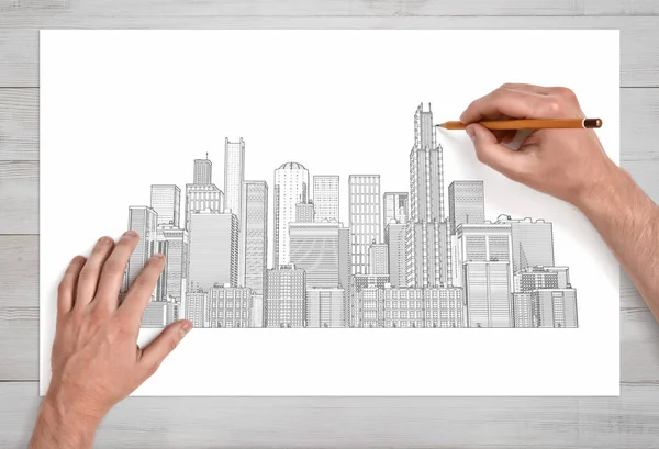 Male hands drawing a city crape with many skyscrapers with a pencil on a white paper in close view.