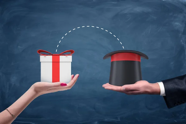 Ένα αρσενικό businessmans χέρι που κρατά ένα καπέλο οδηγούς και ένα γυναικείο χέρι που κρατά ένα κουτί δώρου με τη σύνδεση τελείες μεταξύ. — Φωτογραφία Αρχείου