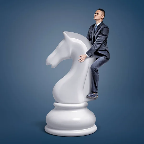Un pequeño hombre de negocios monta una gran pieza de ajedrez blanco sobre un fondo azul . — Foto de Stock