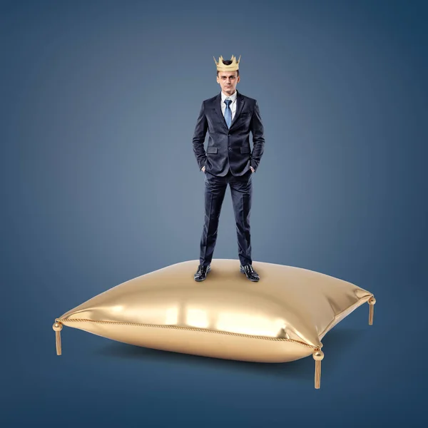 Un hombre de negocios seguro con una corona dorada se levanta sobre un cojín dorado . — Foto de Stock