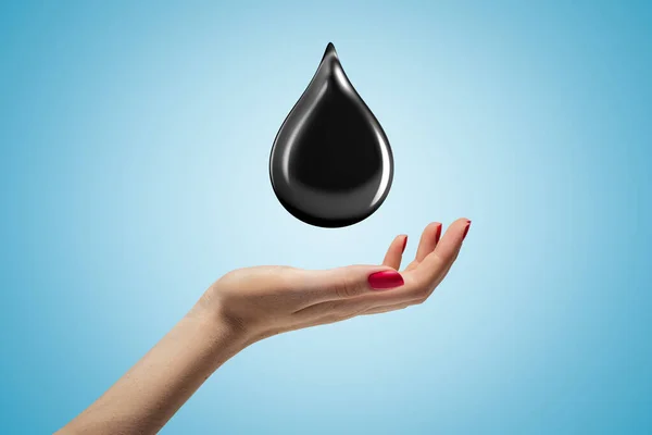 Female hand with black oil drop on blue sky background — ストック写真