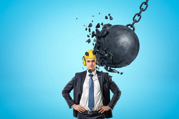 Homme d'affaires portant un casque de sécurité jaune et une boule en métal enchaînée se brisant en morceaux sur fond bleu — Photo