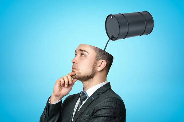 Thinking businessman with black thick liquid spilling out from black oil barrel in his head on blue background — Stockfoto