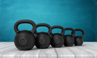 Beyaz ahşap zemin ve koyu turkuaz arka planda üç boyutlu beş adet siyah kettlebell.