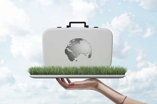 Side view of womans hand holding ipad with green grass growing on screen, and white case with image of Earths continents on, standing on grass.