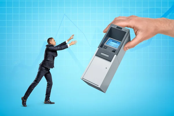 Hatalmas emberek kéz ad miniatűr ATM kis üzletember világoskék háttér enyhén látható üzleti grafikonok. — Stock Fotó