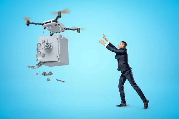 Zakenman heft zijn handen op naar een grote quadcopter die geld draagt, veilig met open deur en geld dat op een blauwe achtergrond valt.. — Stockfoto