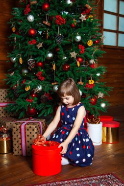 Şaşkınlıkla küçük bir kız hediyesini bir Noel ağacında açar tahta bir kır evinde, yeni yıl, kış mevsimi